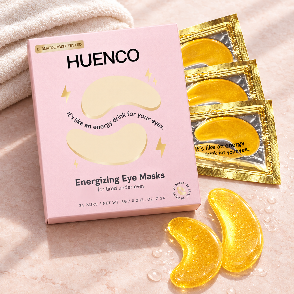  Pink HUENCO eye mask box, gold sachets and two gold gel patches on a blush surface beside an ivory towel.