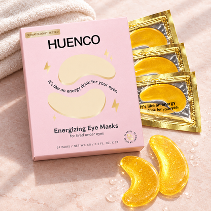  Pink HUENCO eye mask box, gold sachets and two gold gel patches on a blush surface beside an ivory towel.