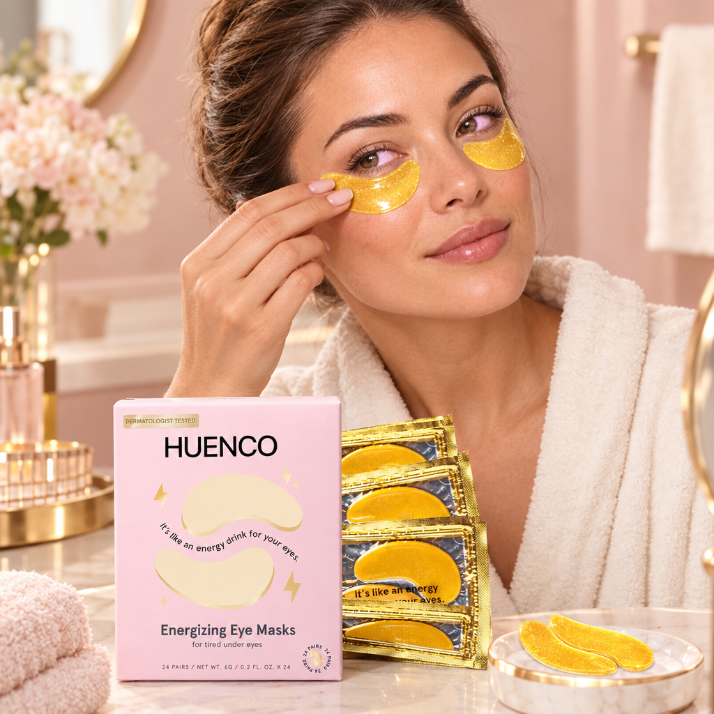 Woman applying a gold under-eye gel patch, with a pink HUENCO box and gold sachets on the vanity.