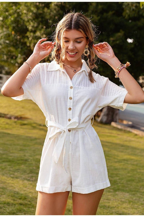 Woman wearing a white romper outdoors with greenery in the background