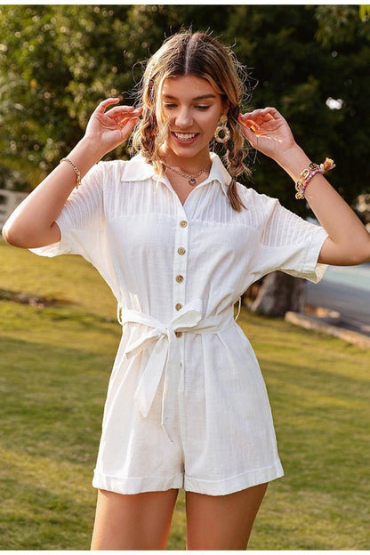 Woman wearing a white romper outdoors with greenery in the background