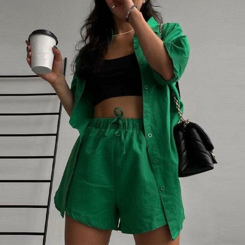 Woman wearing a green outfit with a black top and shorts, holding a coffee cup.