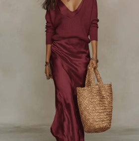 Woman in a burgundy dress holding a woven bag against a neutral background