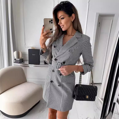 Woman taking a mirror selfie wearing a black and white checkered dress in a modern room.