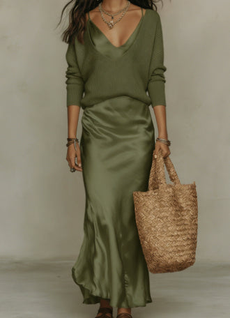 Woman wearing a green outfit holding a woven bag against a neutral background