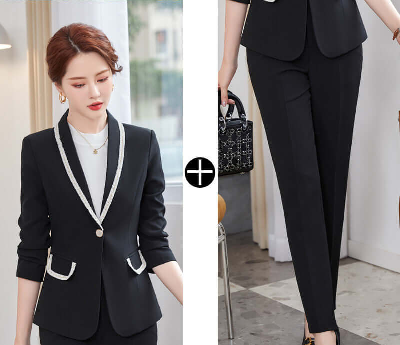 Woman wearing a black suit with white accents, holding a handbag indoors.