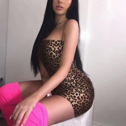 Woman wearing a leopard print bodysuit and pink shorts sitting on a white surface.