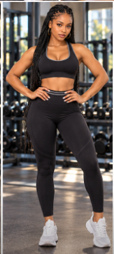 Woman standing with hands on hips in a gym, wearing a black sports bra and matching high-waisted leggings.