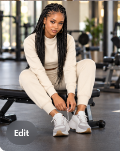 Model seated on a gym bench tying her trainers, wearing an off-white cropped long-sleeve top and matching trousers.
