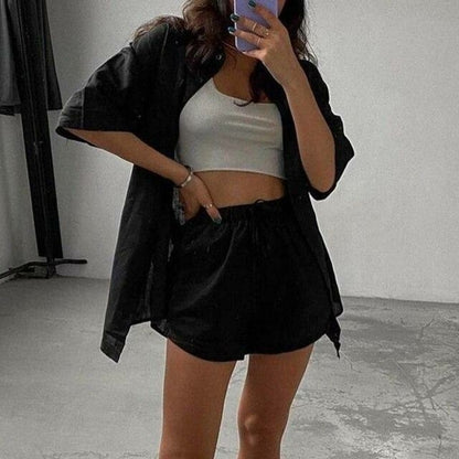 woman wearing a black jacket, white crop top, and black shorts in an indoor setting.