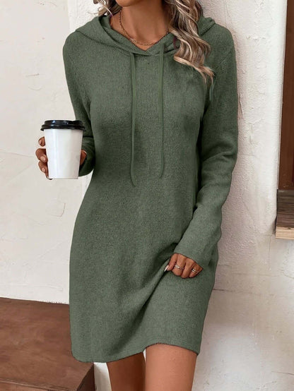 Woman wearing a green hoodie dress holding a coffee cup indoors.
