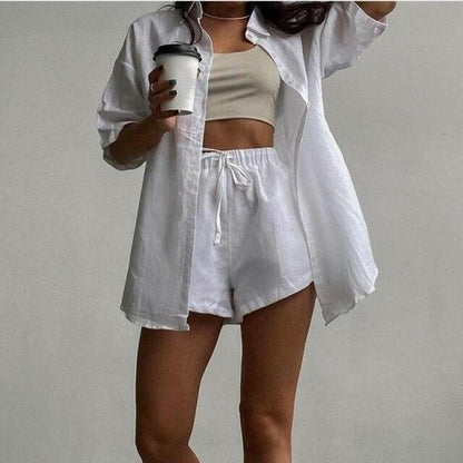 woman wearing a white shirt and shorts holding a coffee cup against a plain background