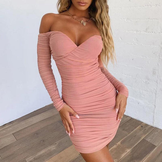 Woman wearing a pink off-shoulder dress against a white brick wall.