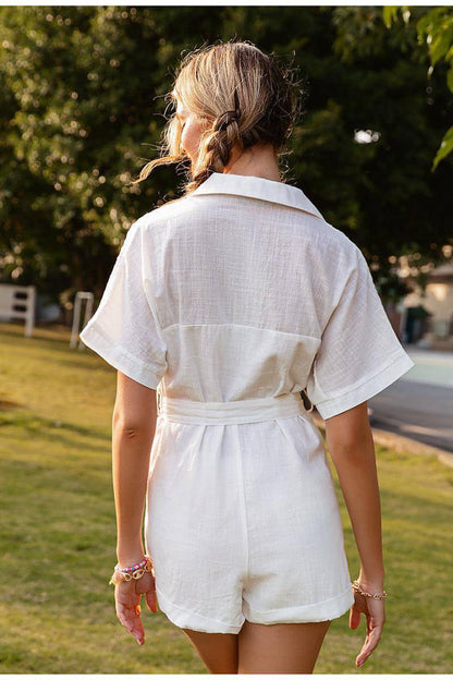 woman wearing a white romper standing outdoors with greenery in the background