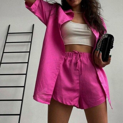 woman wearing a bright pink outfit with a white top and matching skirt, holding a black clutch.