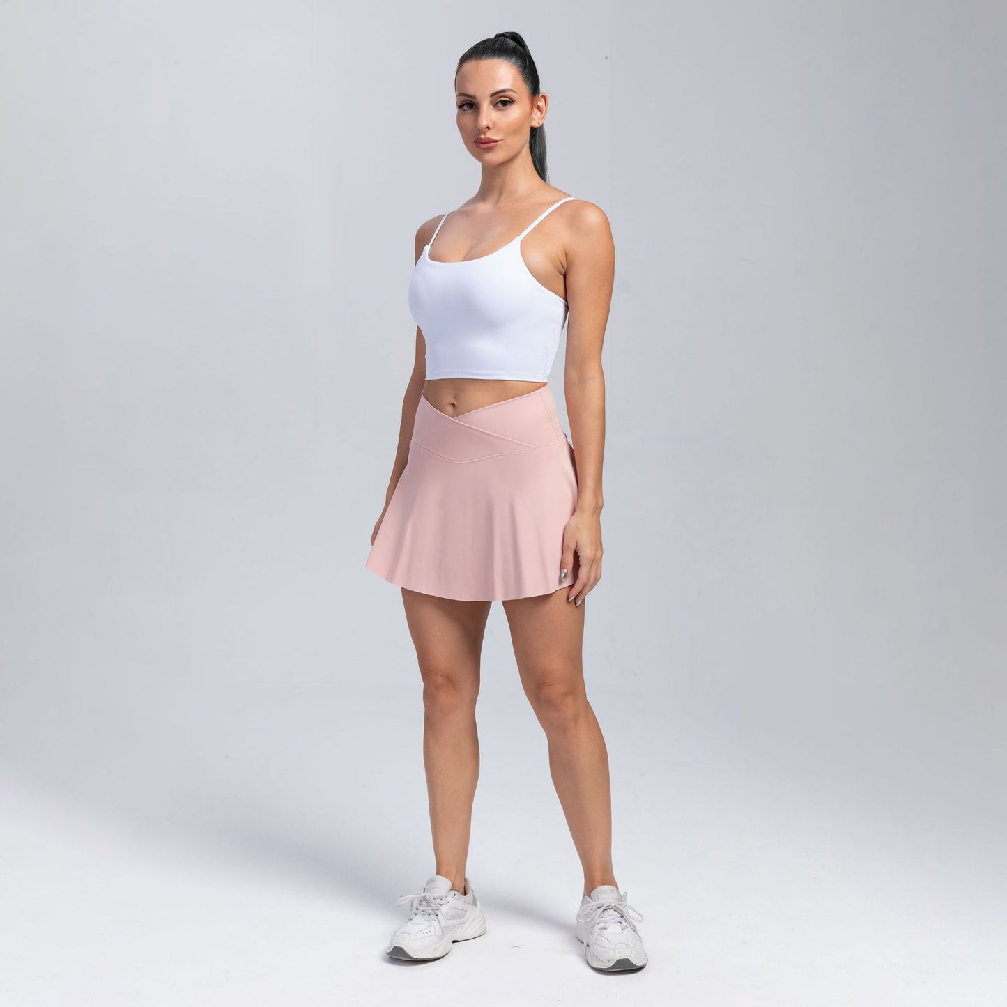 Woman wearing a white tank top and pink skirt on a gray background