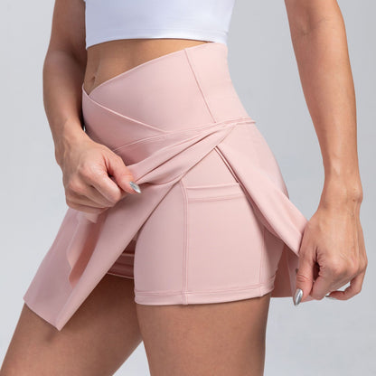 A close-up of a woman wearing high-waisted light pink athletic shorts with a wrap-style front and side pockets, shown against a solid gray background.