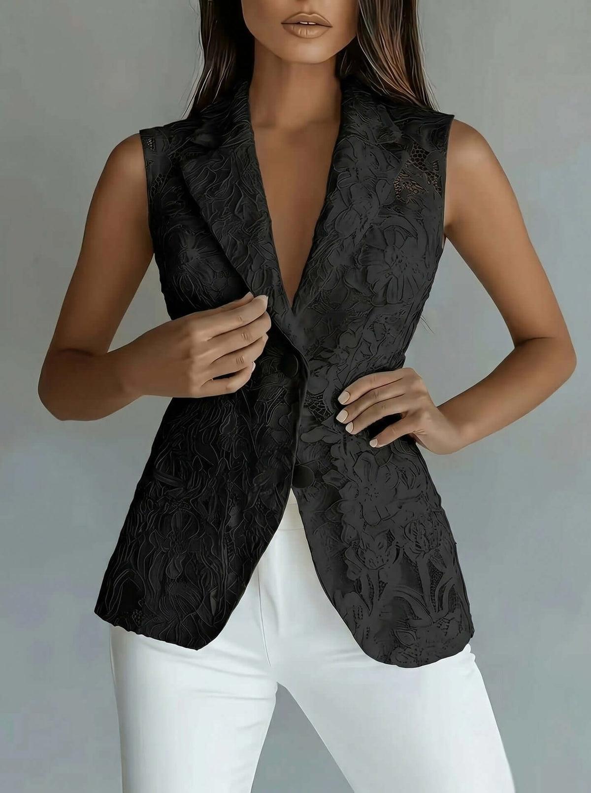 A woman wearing a sleeveless black textured blazer vest with a deep V-neck and white pants, shown from the neck down against a neutral gray studio background.